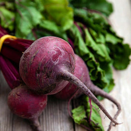 Fresh Detroit Dark Red beets with greens attached, laying on a wooden surface.