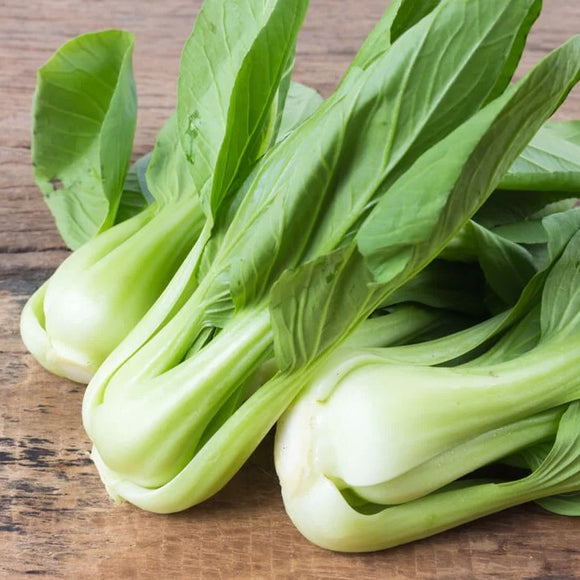 Fresh Bok Choy with vibrant green leaves and thick white stems on a wooden surface.