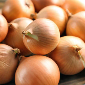 A pile of whole, yellow onions with visible roots on a wooden surface.