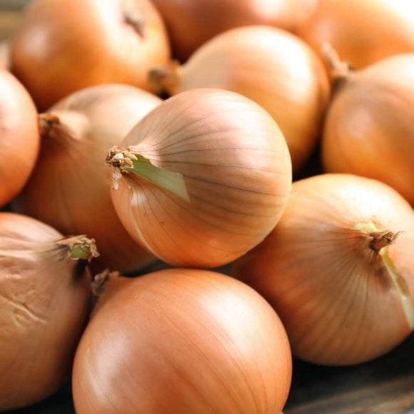 A pile of whole, yellow onions with visible roots on a wooden surface.