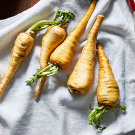 A collection of fresh parsnips with green tops on a light-colored surface.