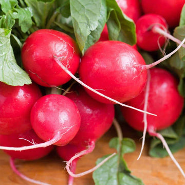 A bunch of red Cherry Belle radishes with green leaves attached, laid out on a wooden surface.