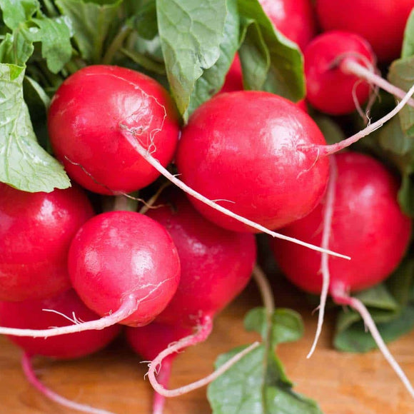 A bunch of red Cherry Belle radishes with green leaves attached, laid out on a wooden surface.