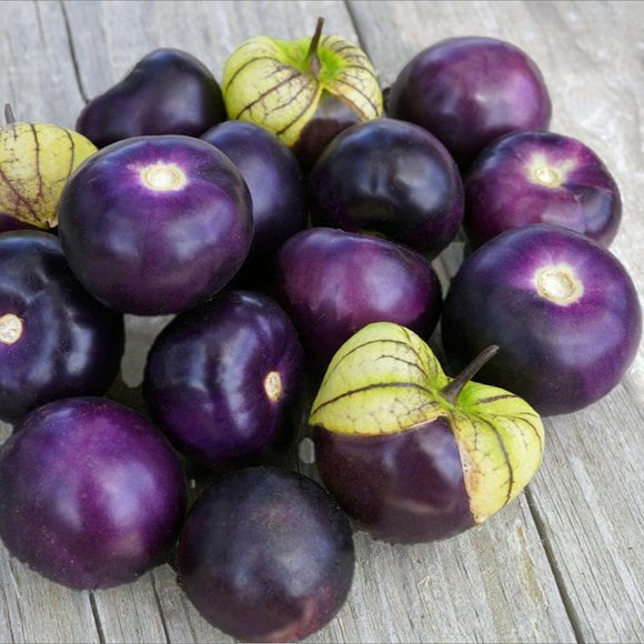 A cluster of purple tomatillos with green tomatillo seeds visible in the center, placed on a wooden surface.