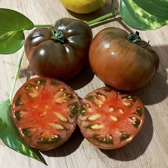 Black tomatoes on a wooden surface with one sliced open to reveal its interior.