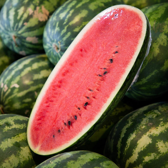 A half slice of watermelon showing the red flesh, with whole watermelons in the background.