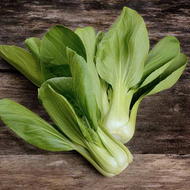 A fresh head of Pak Choi cabbage with thick white ribs and green leaves, placed on a wooden surface.