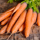 A bunch of fresh Nantes Scarlet carrots with green tops on a wooden surface.