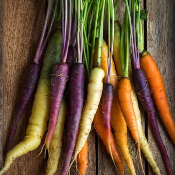 A variety of rainbow blend carrots with different colors including red, purple, yellow, orange, and white, laid out on a wooden surface.