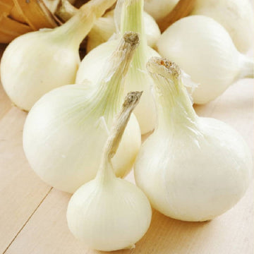 A cluster of white globe onions with stems attached, set on a wooden surface.