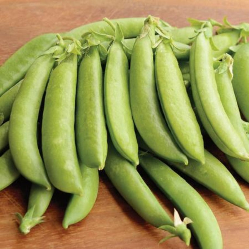 A cluster of fresh green pea pods laid out on a wooden surface.