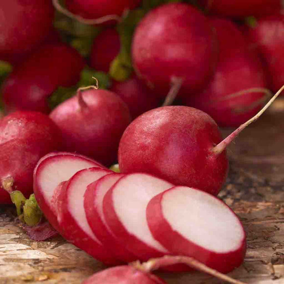 A bunch of fresh radishes with one cut into thin slices, showing the bright red skin and white interior.